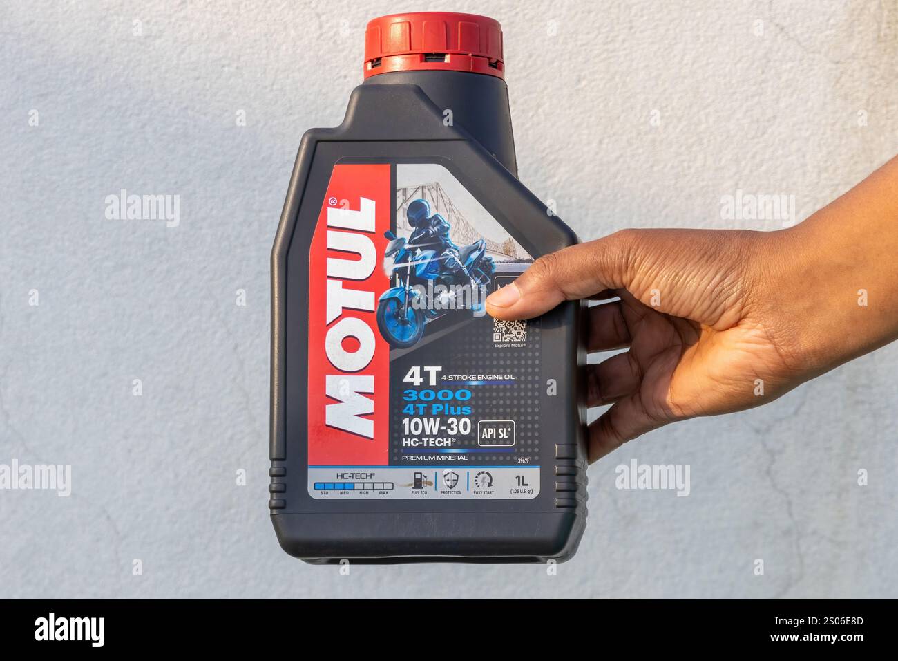 La main d'une femme montre une bouteille d'huile moteur 4 temps minérale Motul 3000 4T plus 10W-30 Premium. Kishoreganj, Bangladesh, 14 décembre 2024. Banque D'Images