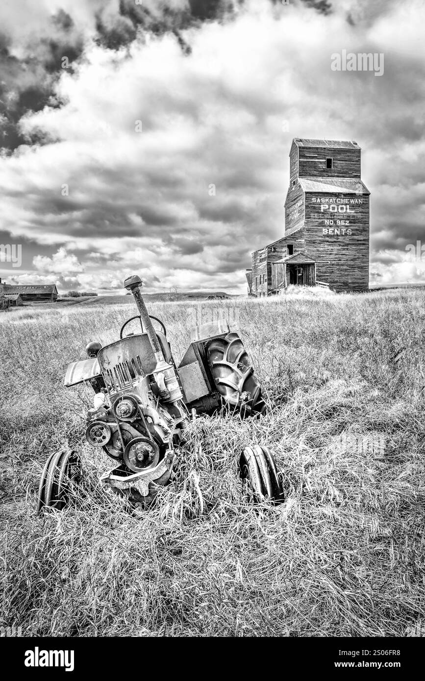 Un tracteur est couché dans l'herbe à côté d'un silo à céréales. Le tracteur est vieux et rouillé. La scène est calme et paisible Banque D'Images