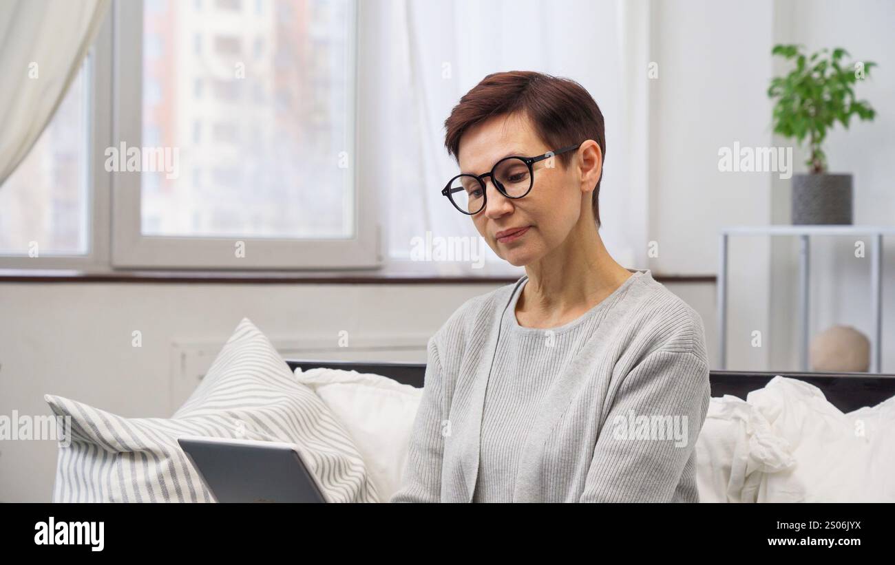 Femme mature avec des lunettes à l'aide d'un ordinateur portable sur un canapé faisant un achat en ligne à la maison Banque D'Images Femme mature avec des lunettes à l'aide d'un ordinateur portable sur un canapé faisant un achat en ligne à la maison Banque D'Images