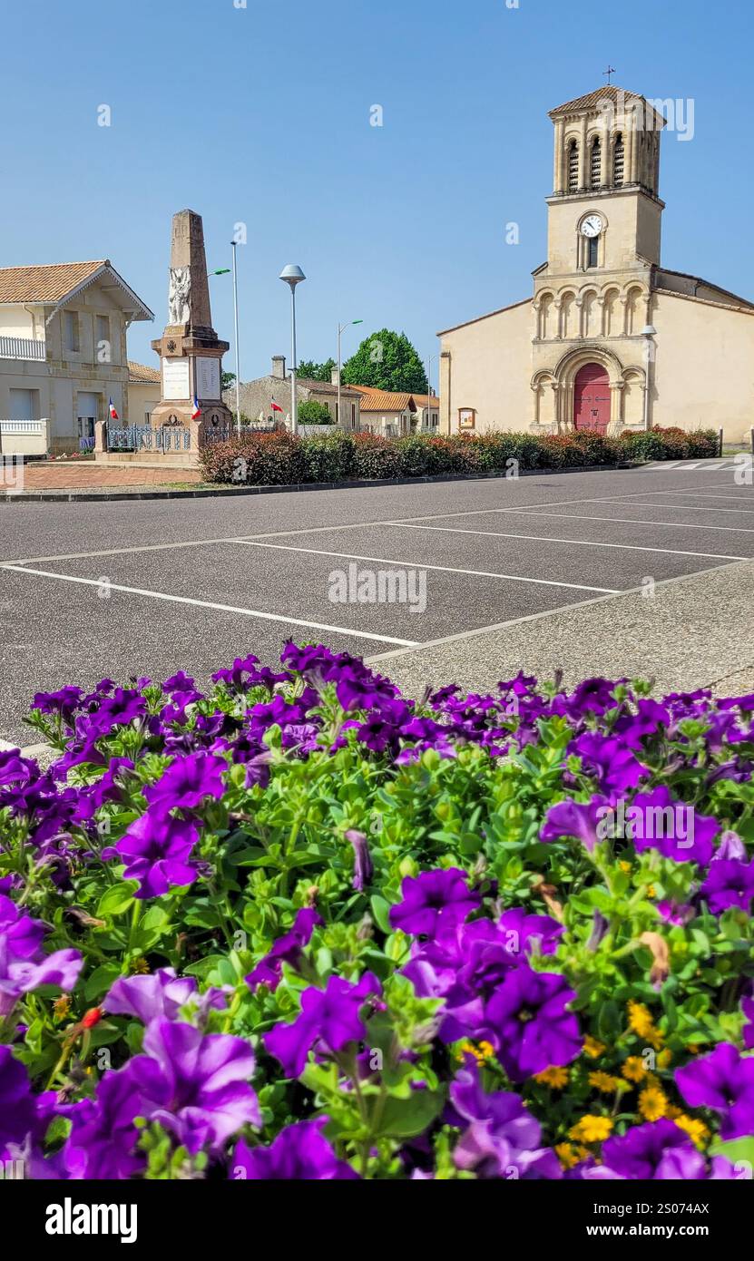 Vue sur la place centrale avec l'église romaine et le monument à la première Guerre mondiale au premier plan - pétunias lilas. Grayan-et-l Hôpital, Nouvell Banque D'Images