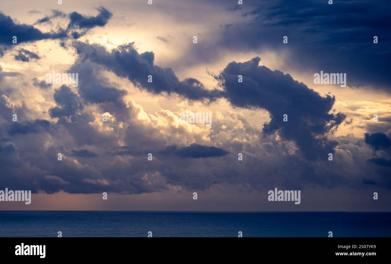Un ciel spectaculaire rempli de nuages sombres et tourbillonnants au-dessus d'un océan calme. Les nuages sont éclairés par une lumière douce, créant un contraste avec le bleu profond s. Banque D'Images