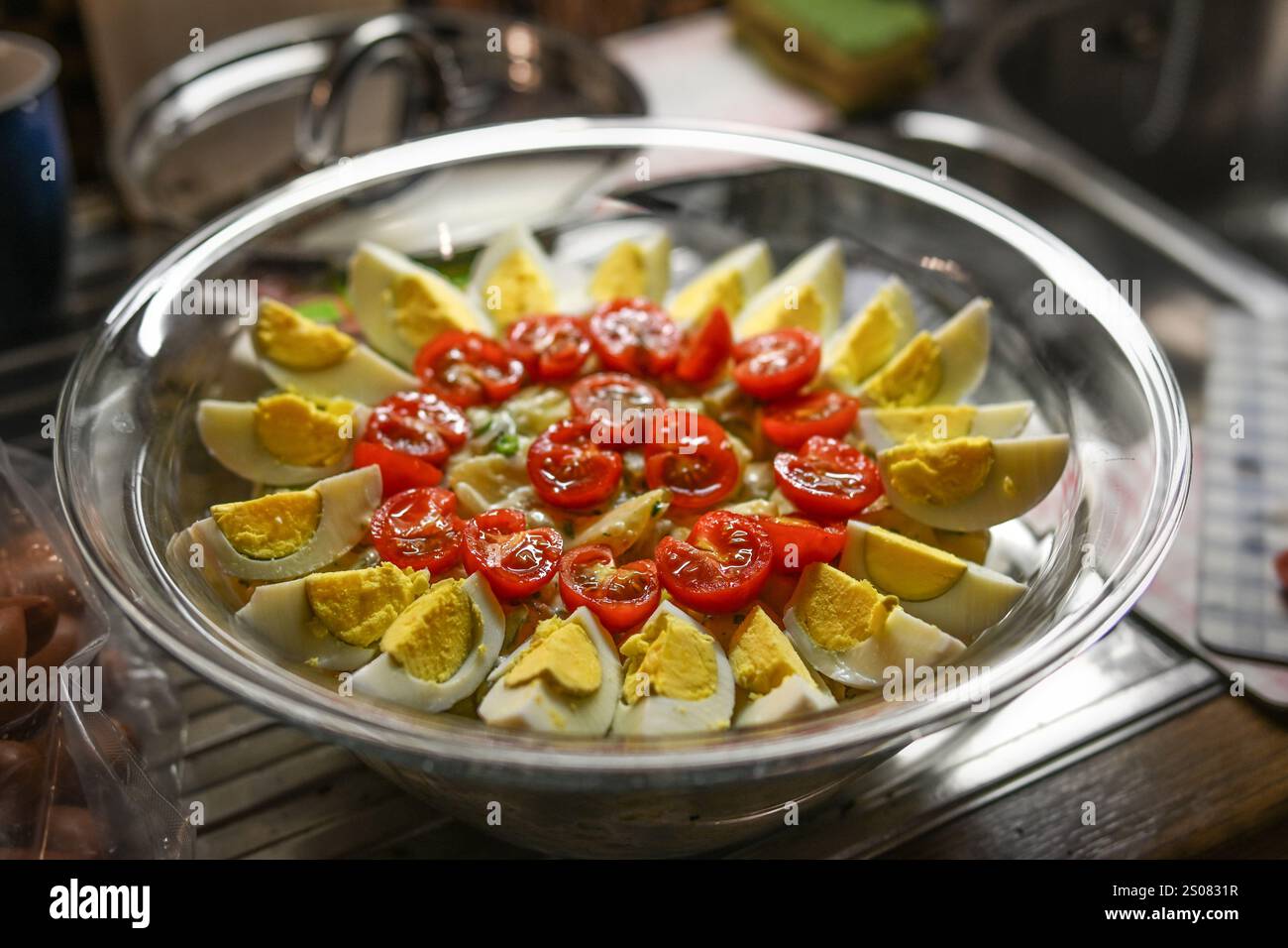 Salade de pommes de terre avec garniture d'œufs en quartiers et tomates cocktail dans un bol en verre dans la cuisine, cuisine maison pour un buffet de fête ou un grand famil Banque D'Images
