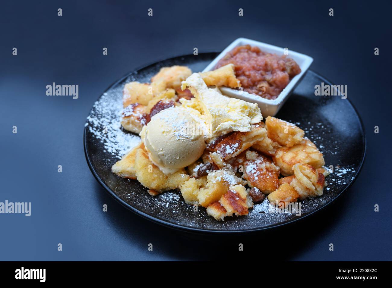 Kaiserschmarrn, crêpe râpée moelleuse avec glace à la vanille et compote de fruits sur une assiette bleu foncé, dessert populaire en Autriche et en Bavière, copie sp Banque D'Images