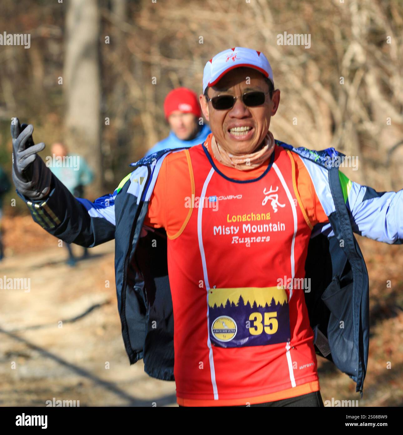 Smithtown, New York, États-Unis - 14 décembre 2024 : un coureur heureux portant une chemise orange lève les bras dans l'excitation tout en courant à travers les bois. Banque D'Images