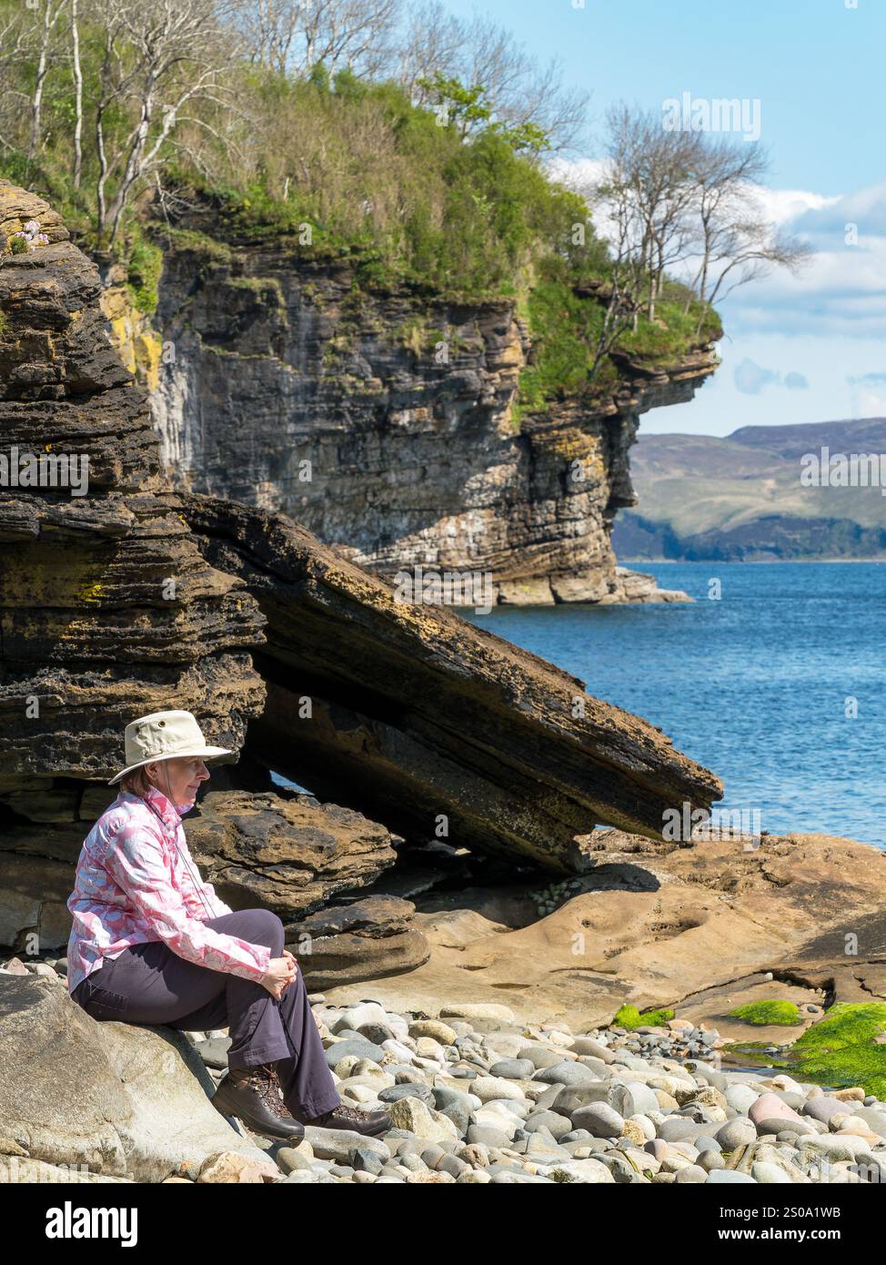 Femme adulte en chapeau de soleil assis sur une plage rocheuse par une journée ensoleillée en mai, Glasnakille près d'Elgol, île de Skye, Écosse, Royaume-Uni Banque D'Images