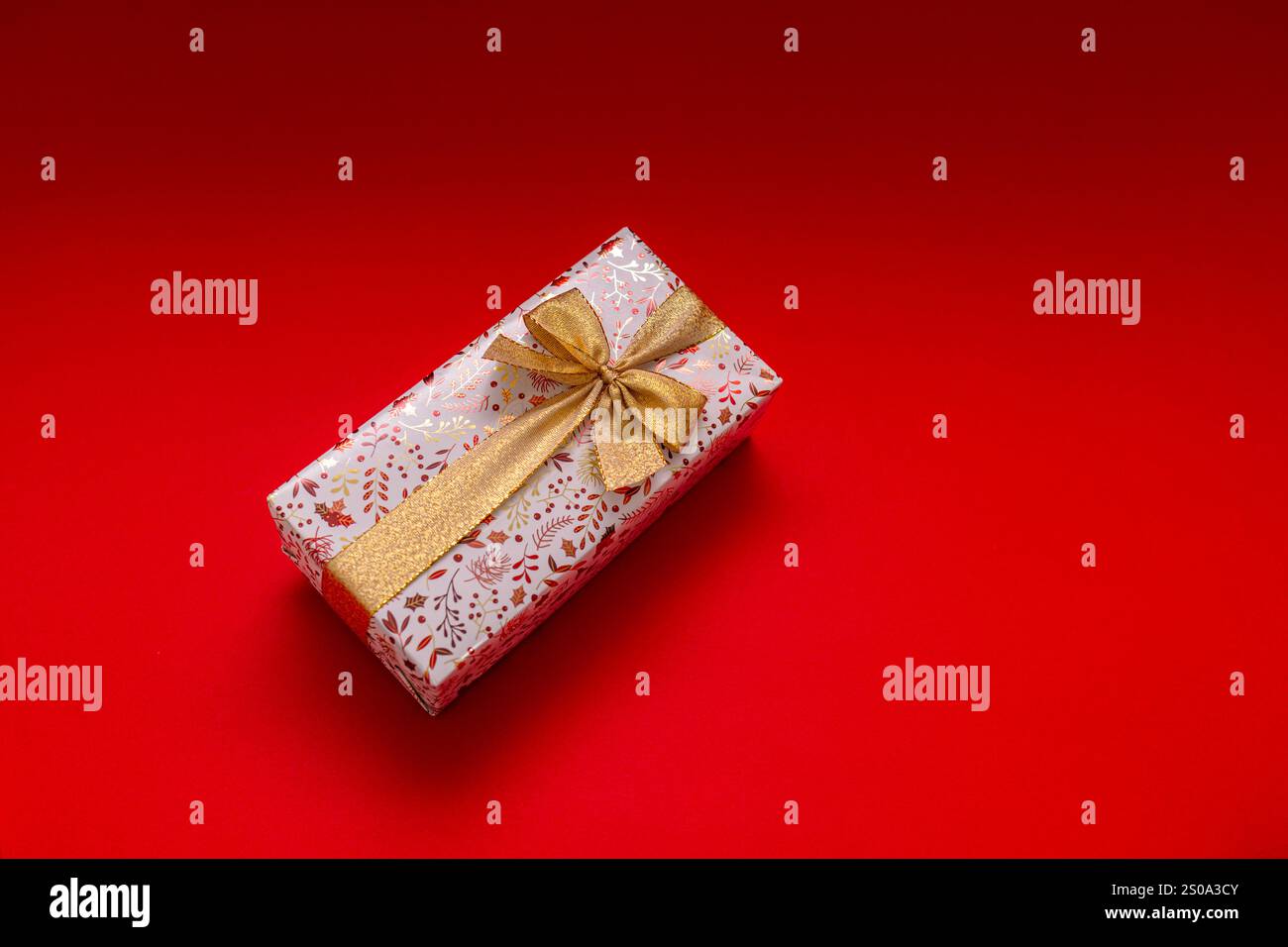 Cadeau enveloppé sur fond rouge vif avec ruban d'or, cadeau d'anniversaire, Saint-Valentin, nouvel an. Le cadeau est doré et brillant Banque D'Images