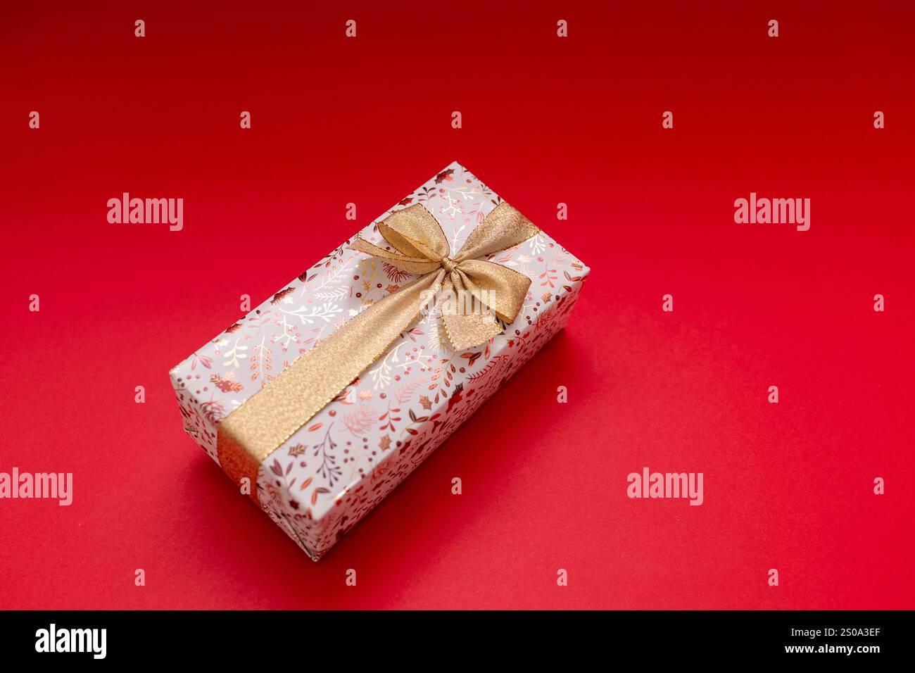 Cadeau enveloppé sur fond rouge vif avec ruban d'or, cadeau d'anniversaire, Saint-Valentin, nouvel an. Le cadeau est doré et brillant Banque D'Images