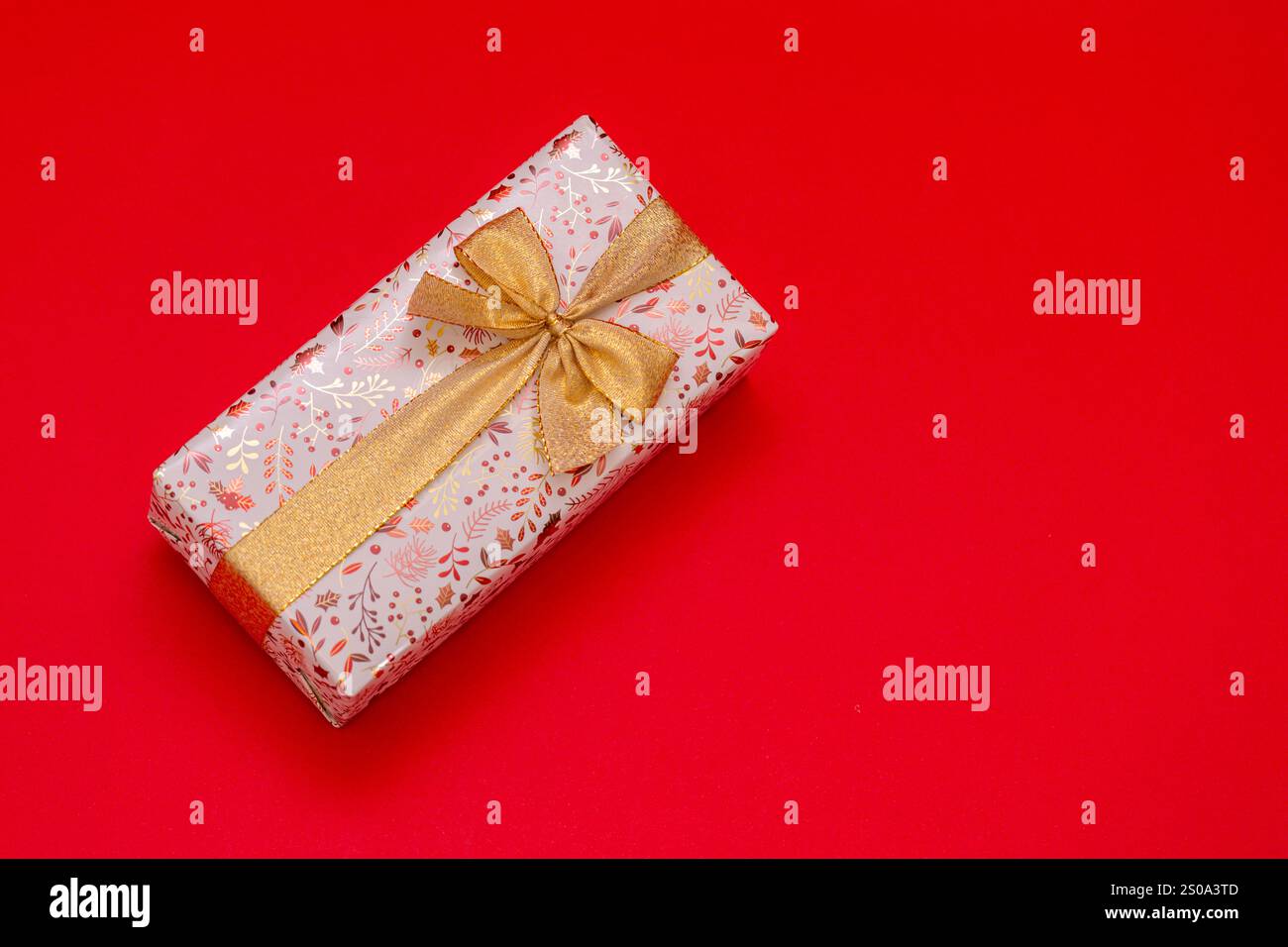 Cadeau enveloppé sur fond rouge vif avec ruban d'or, cadeau d'anniversaire, Saint-Valentin, nouvel an. Le cadeau est doré et brillant Banque D'Images