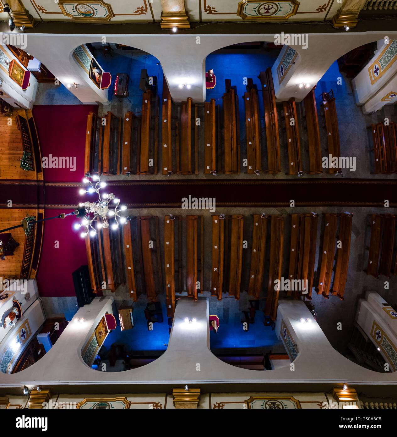 L'image capture une vue aérienne de l'intérieur d'une cathédrale, présentant des bancs en bois symétriques, un lustre central et des détails architecturaux ornés. Banque D'Images