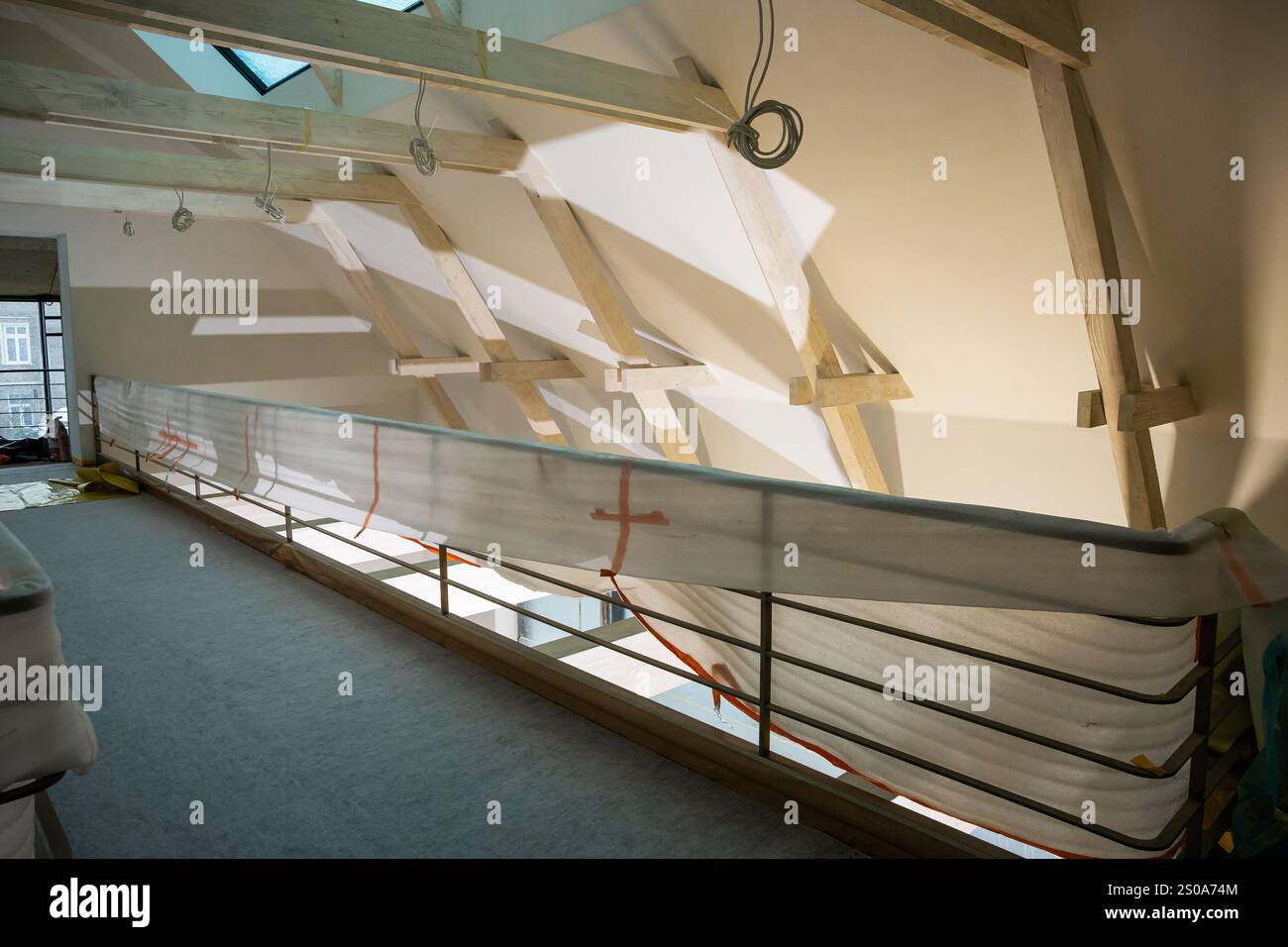 Une zone loft en construction présente des poutres en bois apparentes et un plafond incliné. La lumière naturelle d'une lucarne projette des ombres géométriques sur les murs Banque D'Images