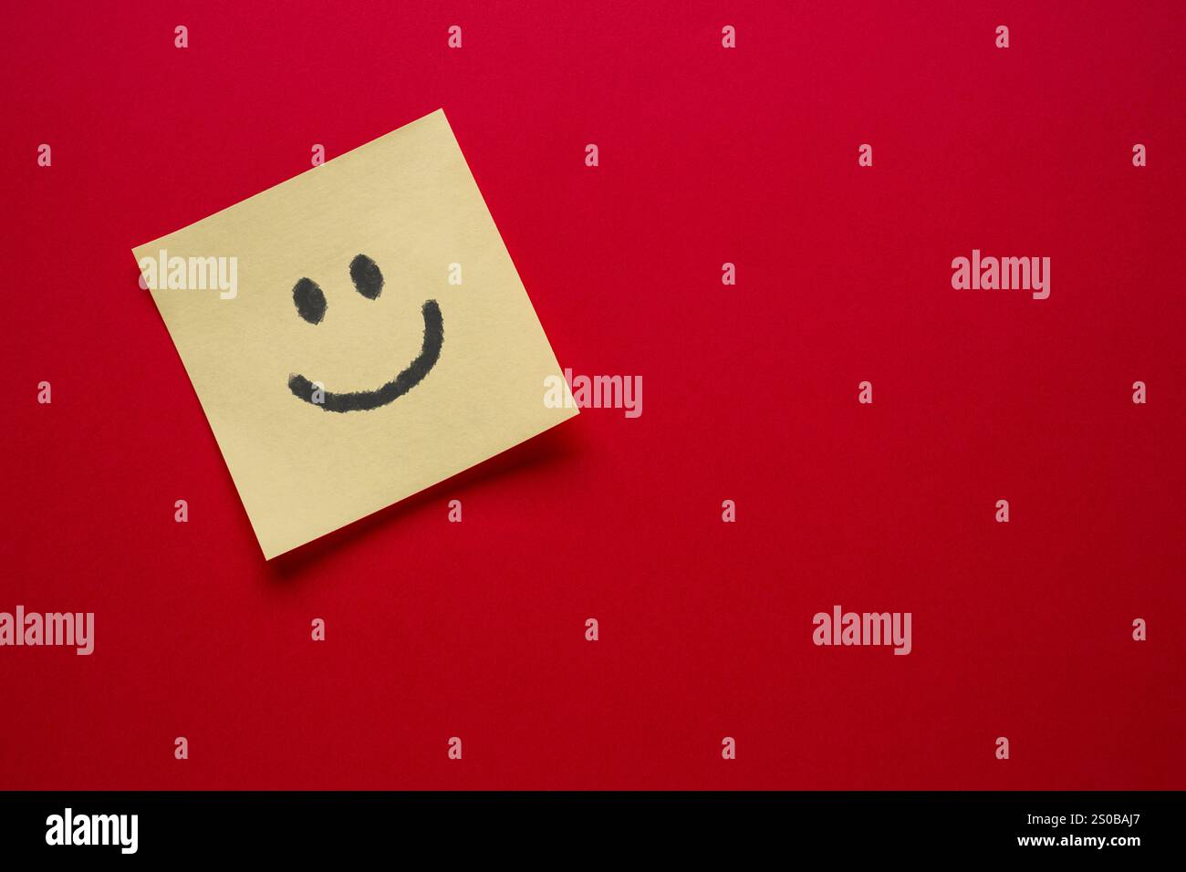 Émoji visage souriant dessin sur papier de note collante sur fond rouge Banque D'Images