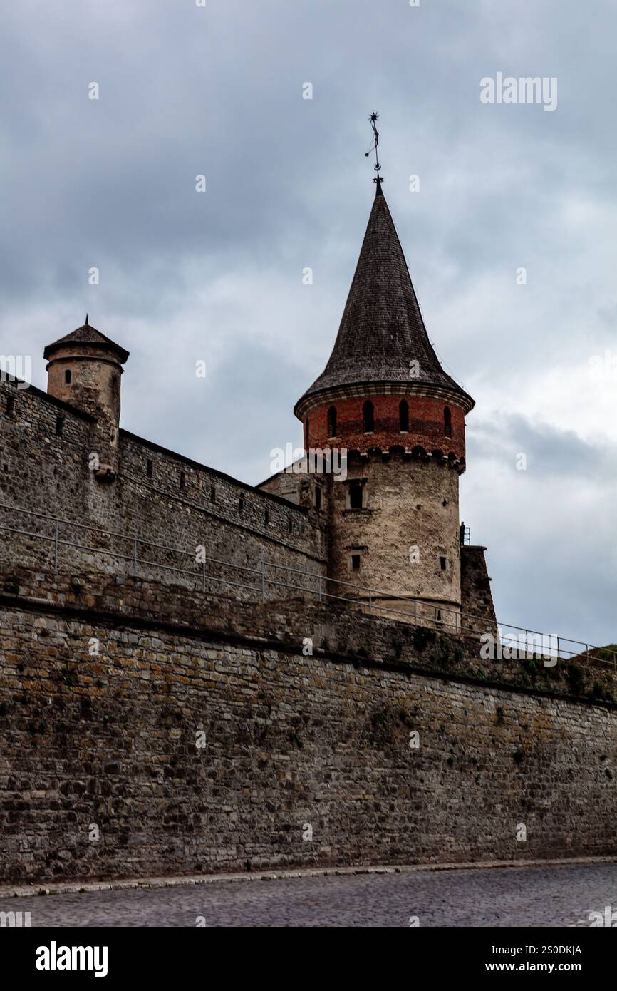 Un château avec un toit rouge et une tour. Le château est entouré d'un mur de pierre. Le ciel est nuageux et le château est en arrière-plan Banque D'Images