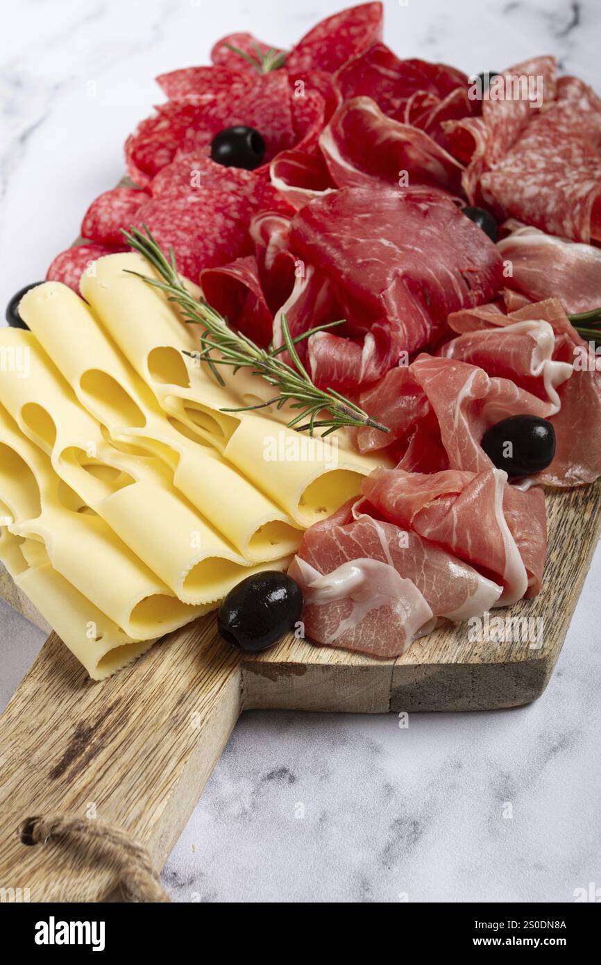 Assortiment de viandes, apéritif, prosciutto, salami et jambon, avec fromage maasdam et olives, sur une planche de bois, petit déjeuner, vue de dessus, gros plan, personne Banque D'Images