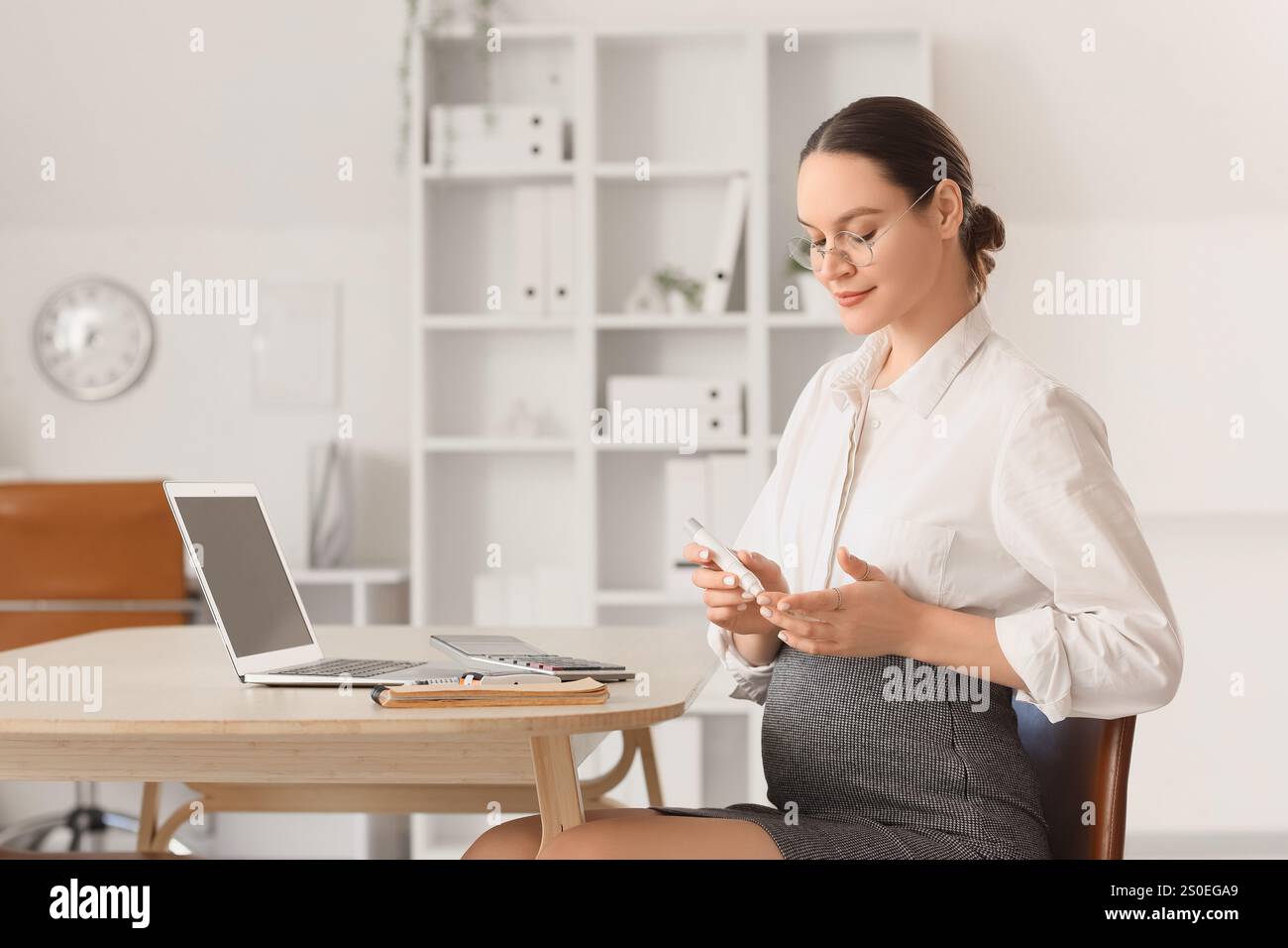 Jeune femme d'affaires enceinte avec diabète gestationnel utilisant un stylo lancette à table dans le bureau Banque D'Images