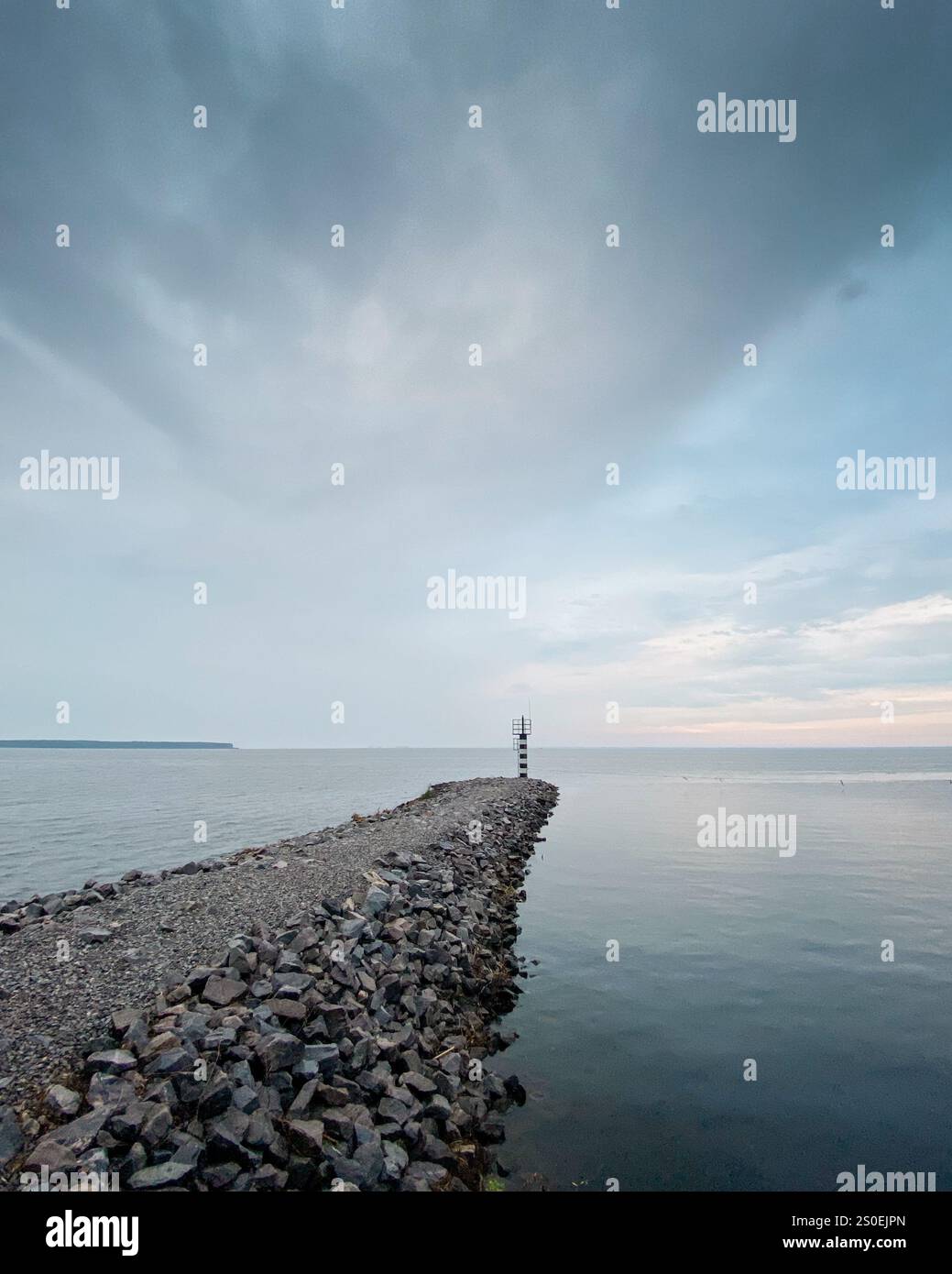 Minuscule phare sur un brise-lames. Vue grand angle du brise-lames en pierre sur une côte de grand lac, temps nuageux. Banque D'Images