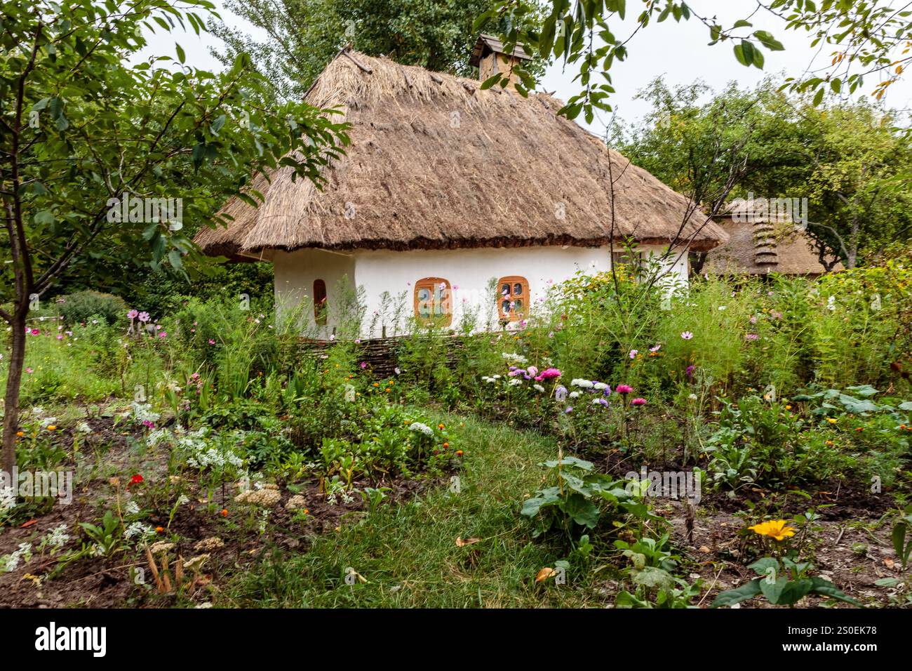 Une petite maison avec un toit de chaume se trouve dans un jardin luxuriant. Le jardin est rempli d'une variété de fleurs et de plantes, créant un calme et serein à Banque D'Images