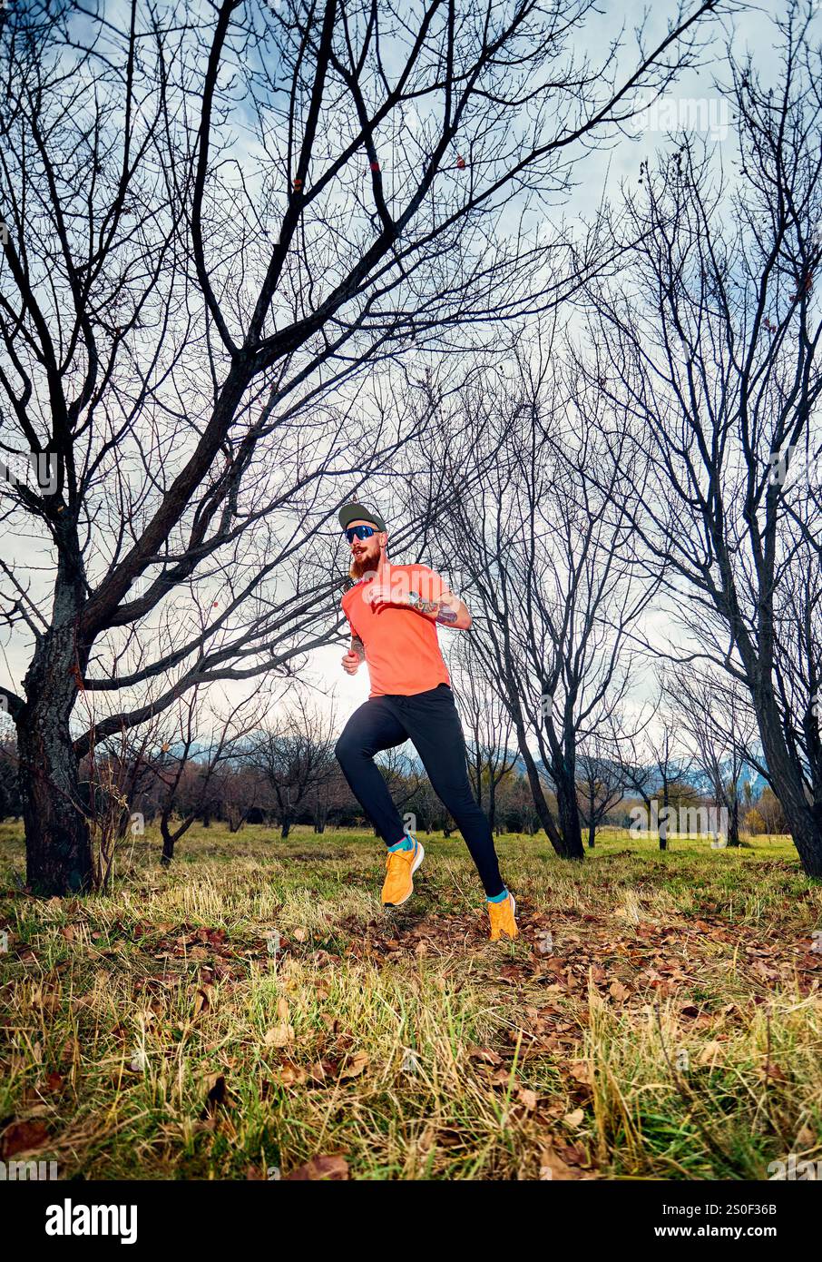 Homme barbu athlétique en chemise rouge courant sur le sentier de sentier dans la forêt d'automne au lever du soleil Banque D'Images