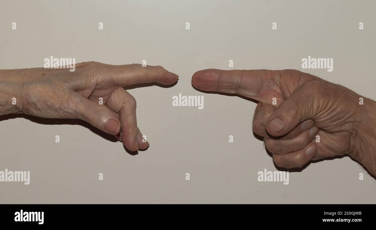 Image en gros plan de deux mains âgées, avec les doigts tendus, pointant l'une vers l'autre sur un fond Uni, symbolisant un geste doux de Banque D'Images