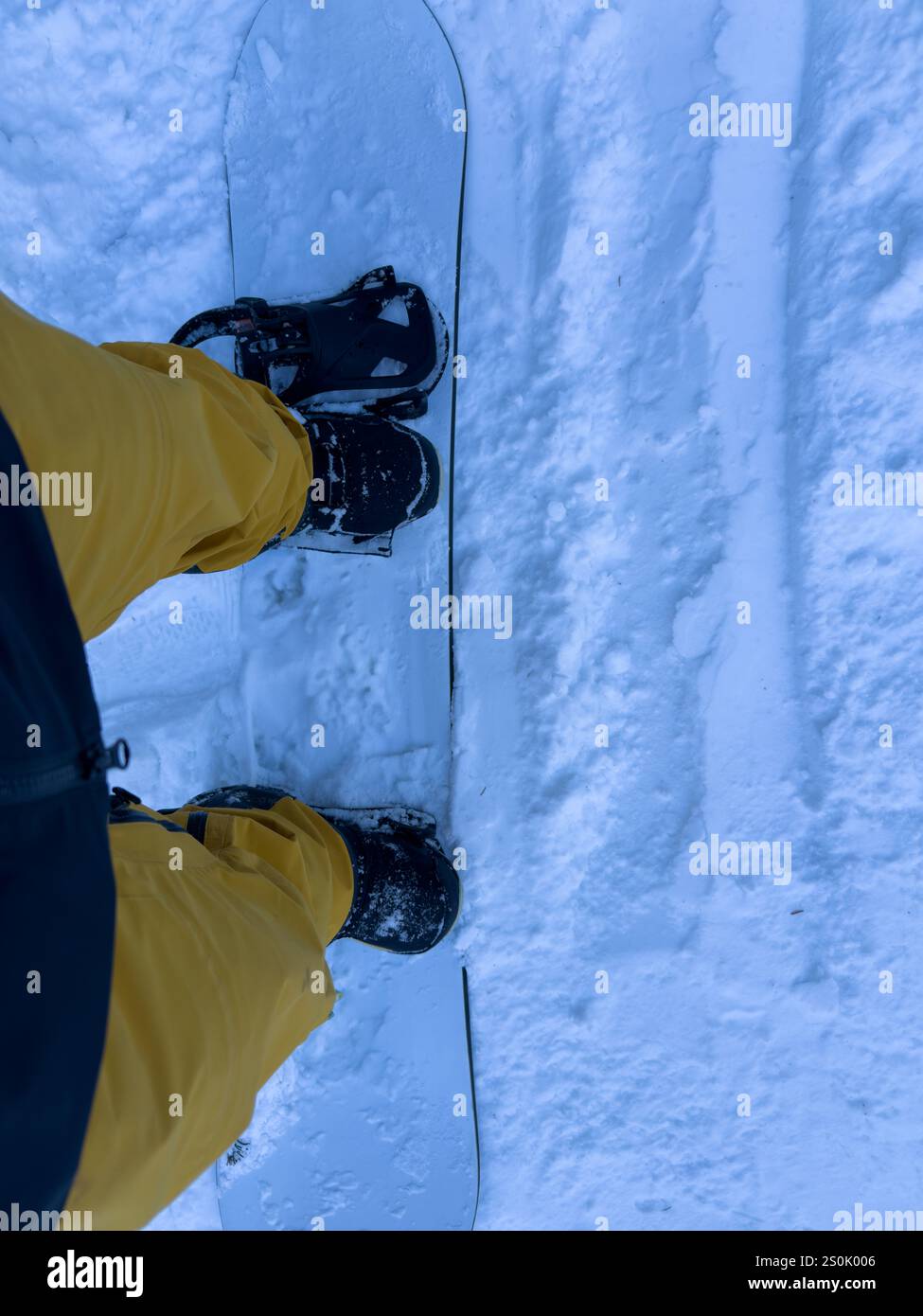 Photo d'un snowboardeur en pantalon jaune et bottes noires sur une pente enneigée. Banque D'Images