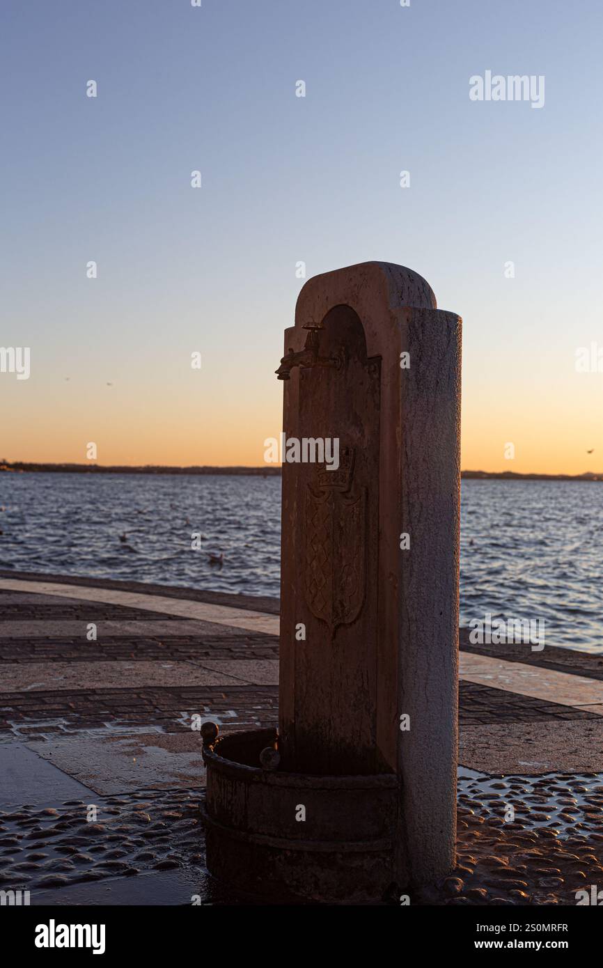 Fontaine en pierre ou monument sur le trottoir du front de mer. Lumière chaude sur le détail architectural par l'eau. Banque D'Images Fontaine en pierre ou monument sur le trottoir du front de mer. Lumière chaude sur le détail architectural par l'eau. Banque D'Images