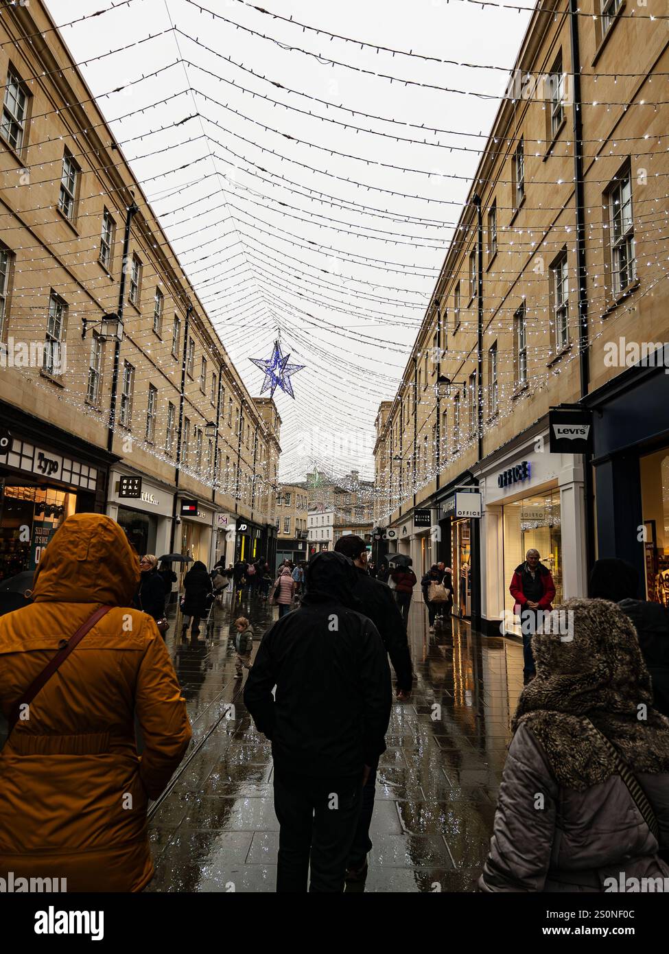 Les gens marchant le long d'une rue commerçante en plein air étroite sous les lumières de vacances un jour de pluie Southgate Bath UK Dec 2024 - Image de stock capturée avec un smartphone