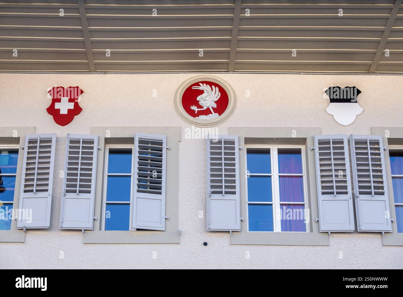 Gruyères, Suisse - 21 septembre 2024 : volets gris sur les fenêtres, et emblèmes décoratifs de la Suisse, Gruyères et Fribourg. Banque D'Images