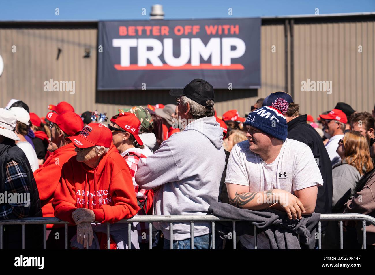 Les partisans de Trump se tiennent dans une foule avec un grand panneau TRUMP accroché à un bâtiment en arrière-plan lors d’un rassemblement en plein air. Banque D'Images