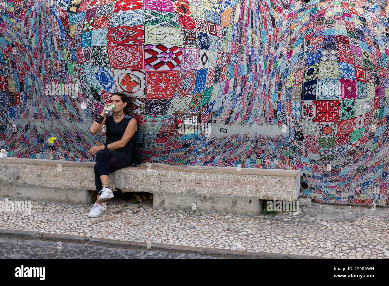 Femme assise sur un banc avec une mosaïque colorée derrière elle dans la tendance LX Factory, Lisbonne, Portugal Banque D'Images