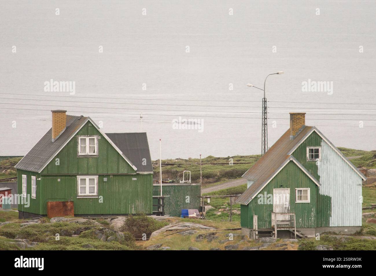 Une maison verte pittoresque à Qeqertarsuaq, au Groenland, sur fond d'océan Arctique. Le dos d’une baleine émerge gracieusement du Wat glacé Banque D'Images