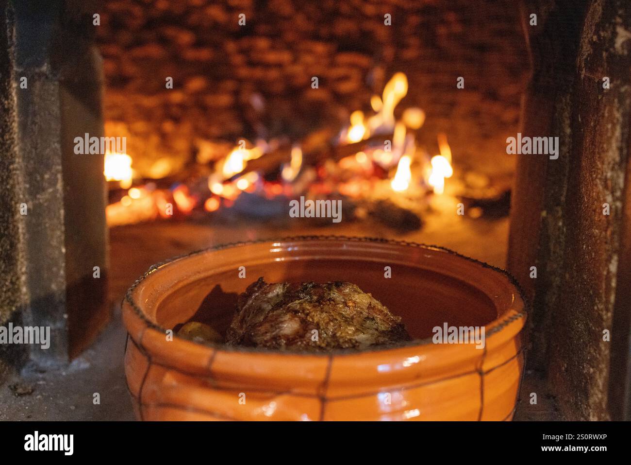 Gros plan d'un pot en argile avec un repas fraîchement cuit à l'intérieur d'un four à bois, brillant de flammes chaudes en arrière-plan. Banque D'Images