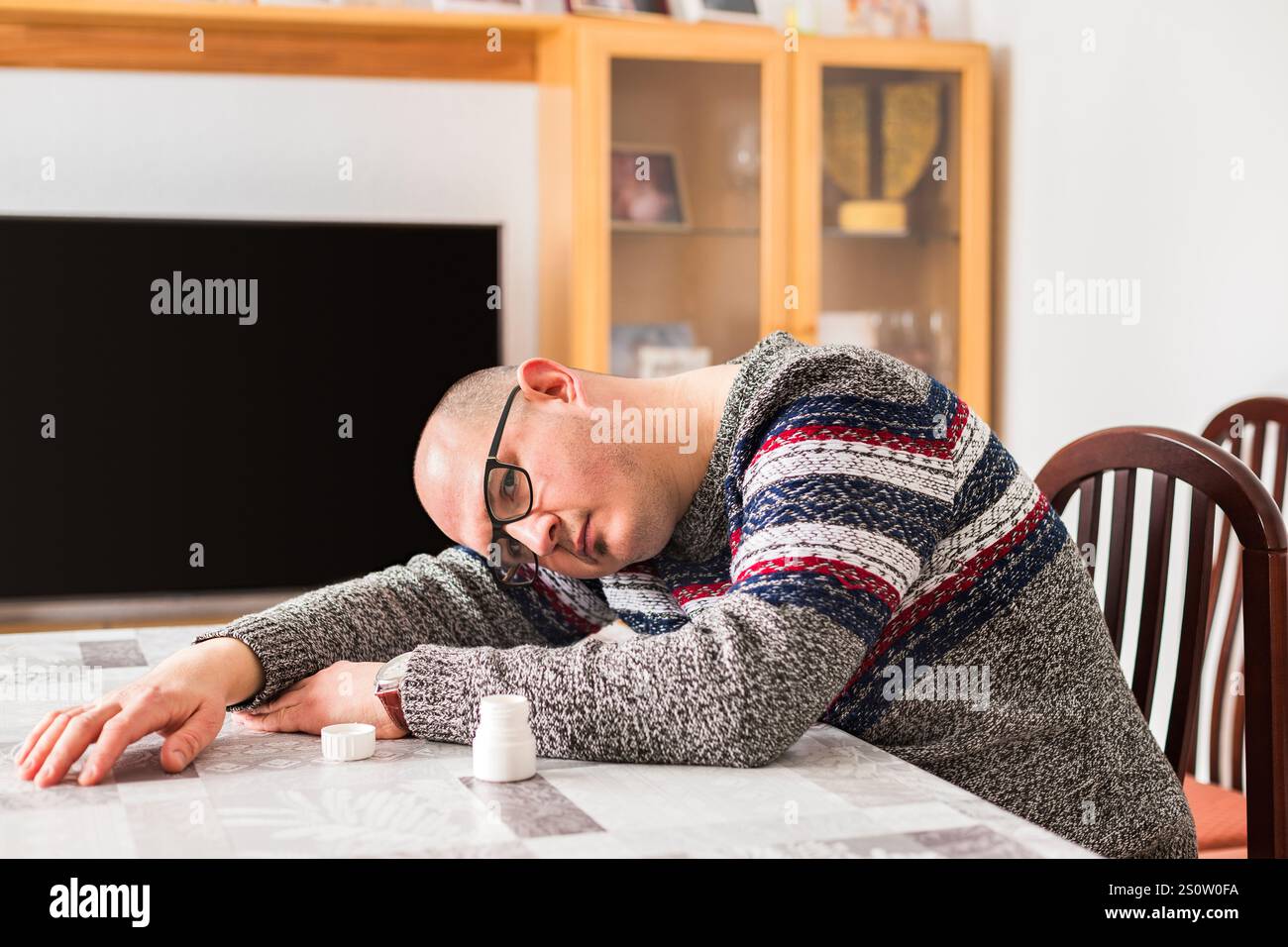 Un homme adulte chauve assis à côté d'une table et couché sur elle, abîmé et déchiré, reposant sa tête sur un de ses bras avec un visage triste, à côté d'un moi Banque D'Images