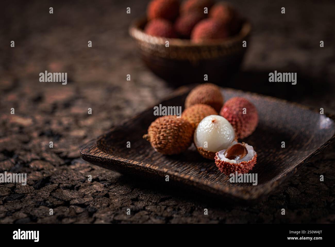 Les litchis frais sont servis sur un plateau en bois, présentant leur chair blanche et leurs graines foncées, avec plus de litchis dans un bol en arrière-plan Banque D'Images