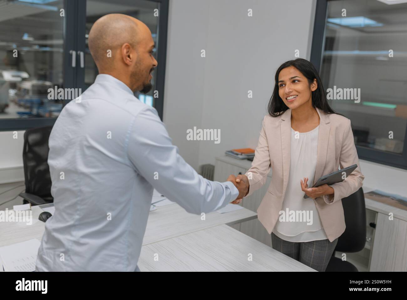 Femme indienne, chef d'entreprise prospère serrant la main d'un candidat à un emploi, un jeune homme afro-américain, après un entretien d'embauche réussi. Banque D'Images