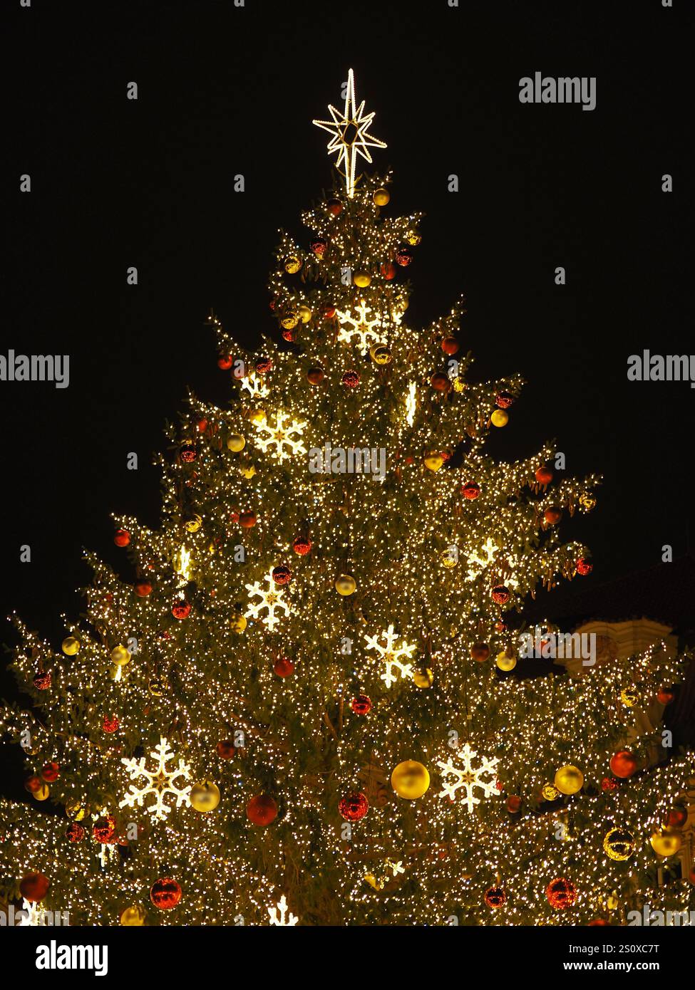 Sapin de Noël brillamment éclairé avec des ornements dorés, des boules rouges et des flocons de neige illuminés sur la place de Prague. Banque D'Images