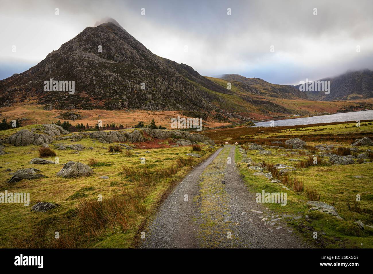 Paysage spectaculaire avec une route de gravier menant à un lac avec des montagnes majestueuses en arrière-plan sous ciel nuageux Banque D'Images