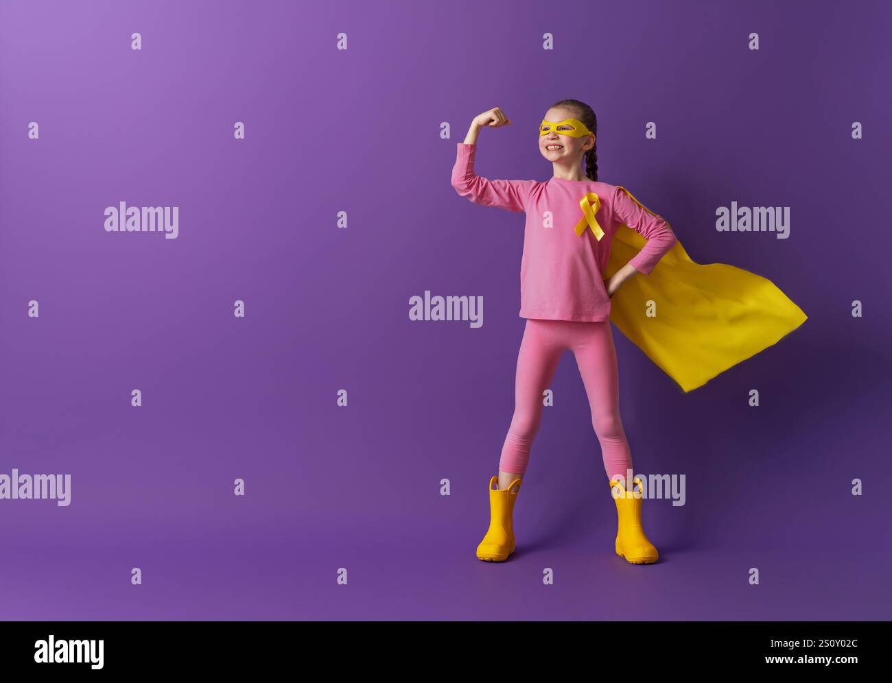 Journée mondiale du cancer de l'enfance.Fille en costume de super-héros avec ruban doré. Banque D'Images