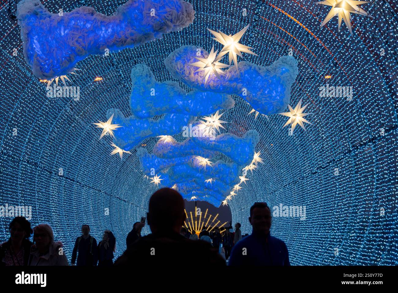 Une scène nocturne d'un tunnel lumineux vibrant avec des étoiles brillantes et des décorations de nuages, créant une atmosphère enchanteresse. Silhouettes de personnes wa Banque D'Images
