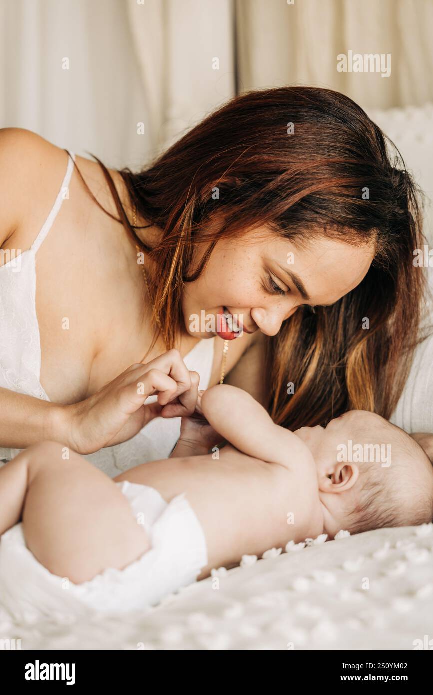 Mère souriant tendrement avec son bébé sur un lit moelleux et douillet Banque D'Images