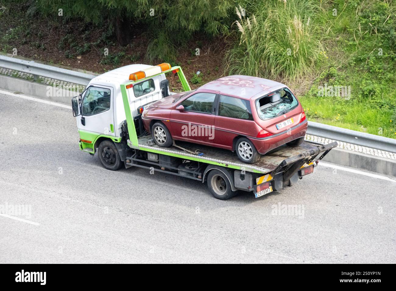 La dépanneuse transporte une voiture rouge endommagée avec une lunette arrière cassée sur une autoroute Banque D'Images