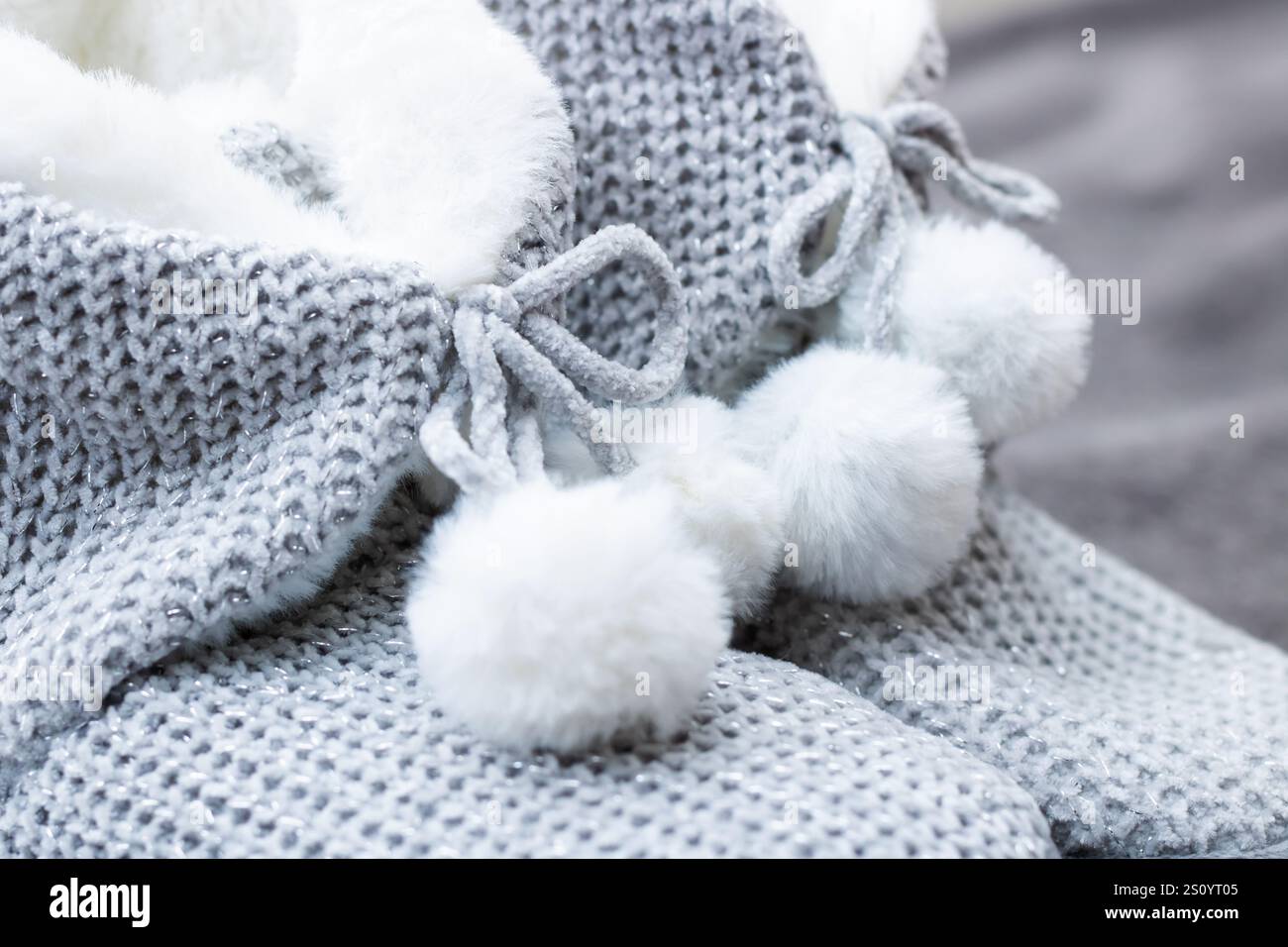 Une paire confortable de chaussons tricotés ornés de charmants pompons blancs repose sur un lit moelleux, créant une atmosphère chaleureuse Banque D'Images