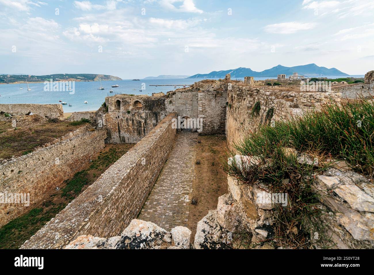 Vue panoramique sur les murs de la forteresse de Methoni, mettant en valeur les bastions, la porte voûtée, et une magnifique toile de fond de la mer avec des bateaux ancrés. Banque D'Images