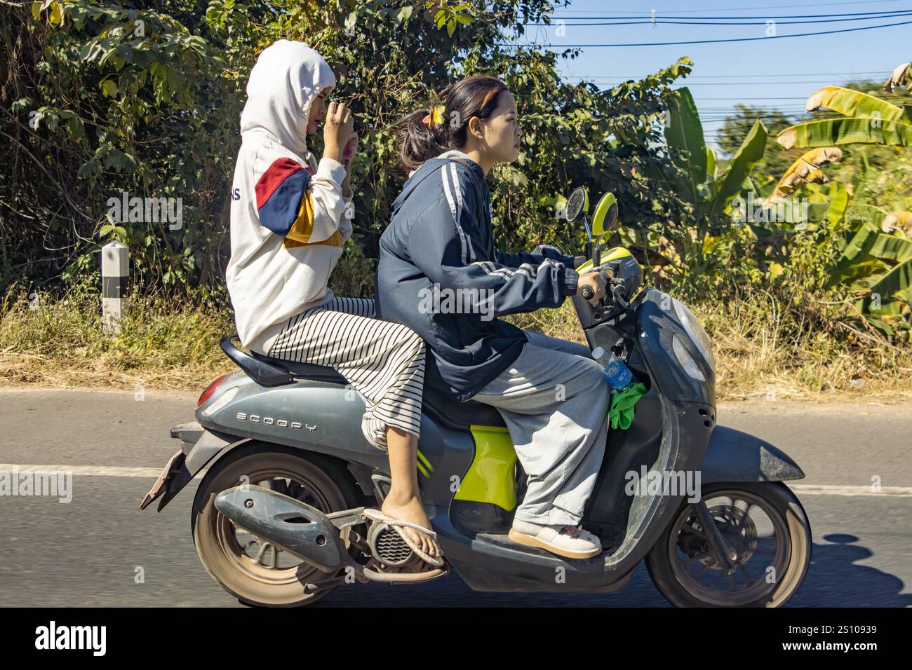 UBON RATCHATHANI, THAÏLANDE, 17 décembre 2024, Une paire de femmes conduisant une moto sur une route de campagne Banque D'Images