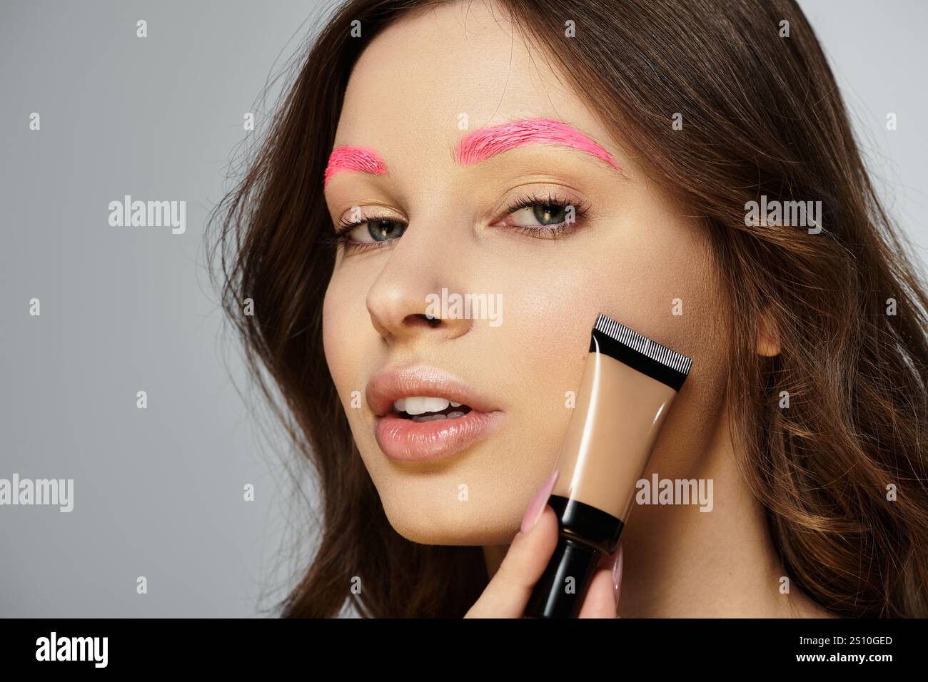 Jeune femme montre sa beauté frappante avec des sourcils roses vibrants sur un fond gris. Banque D'Images