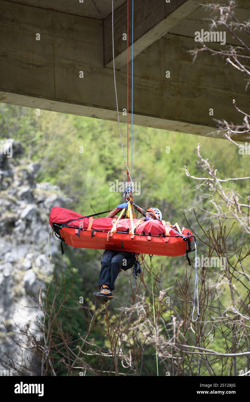 Secouriste d'urgence abaissant la civière et l'équipement avec système de corde par temps ensoleillé Banque D'Images