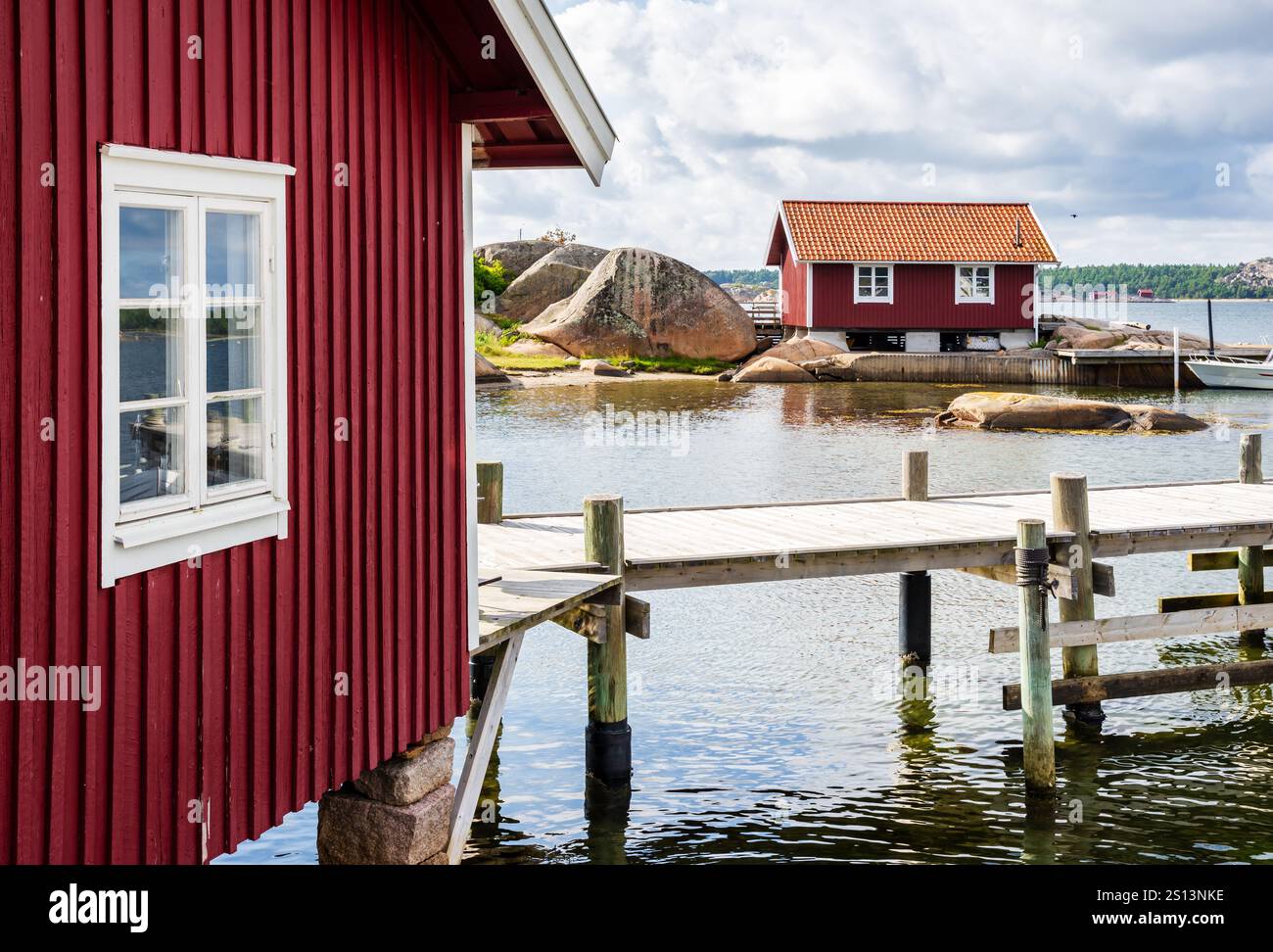 Deux cabanes à bateaux peintes en rouge et une jetée en bois sur la côte de granit rose dans la province de Bohuslän, en Suède, sous un ciel orageux par une journée d'été ensoleillée. Banque D'Images
