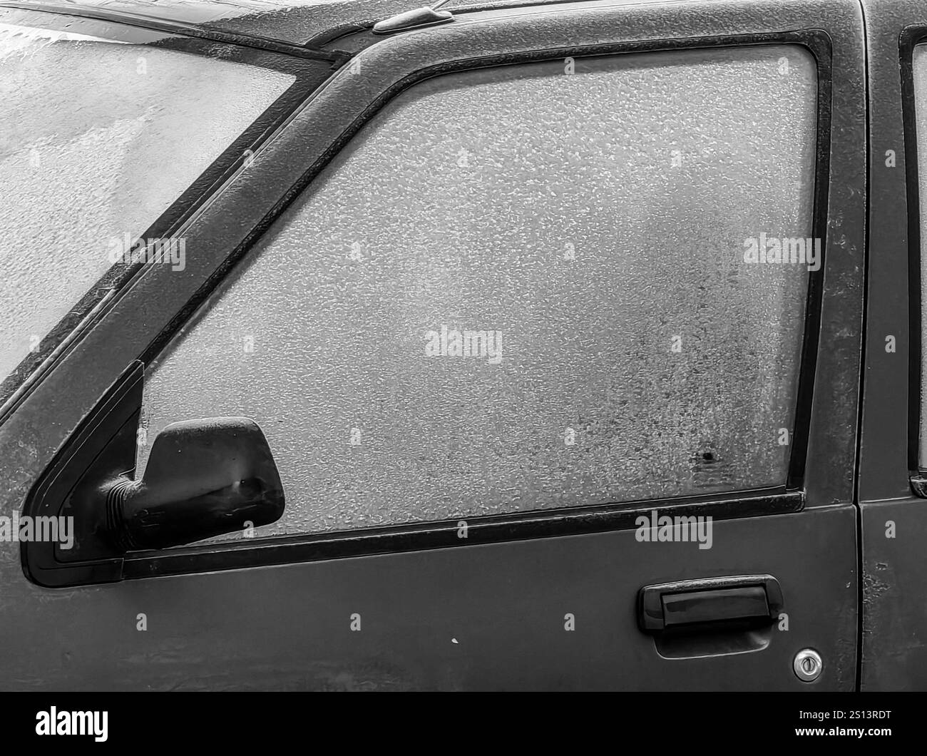 Motifs gelés : verre givré et poignée d'une voiture en stationnement, avec rétroviseur arrière gauche. Banque D'Images