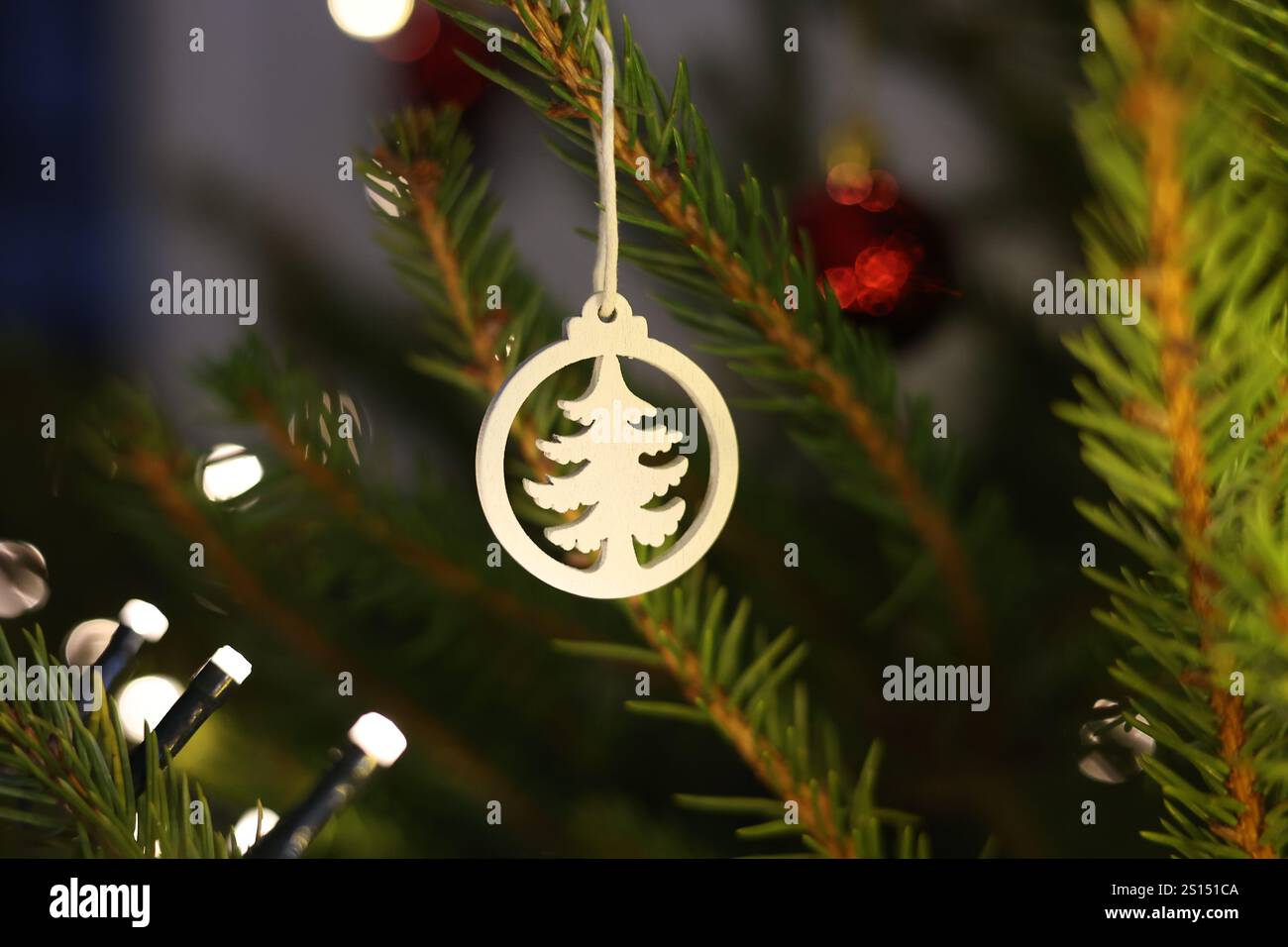 Ornement blanc, naturel, en forme d'arbre suspendu sur un arbre de Noël avec des lumières de fées chaudes en arrière-plan Banque D'Images