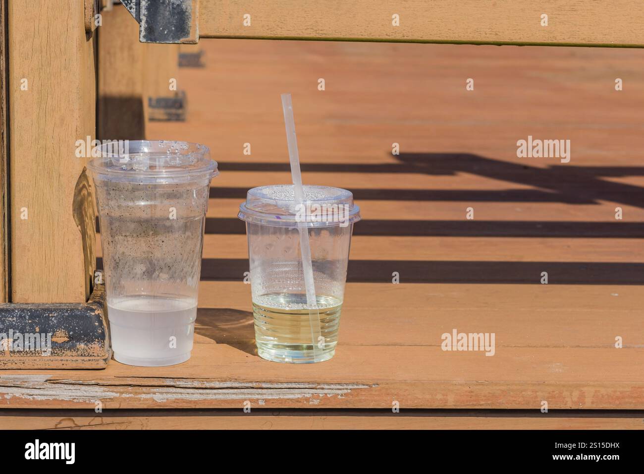 Deux gobelets en plastique sur une surface en bois à la lumière du soleil, projetant des ombres avec des liquides clairs et verts à l'intérieur, situé à Wando, Corée du Sud, Asie Banque D'Images