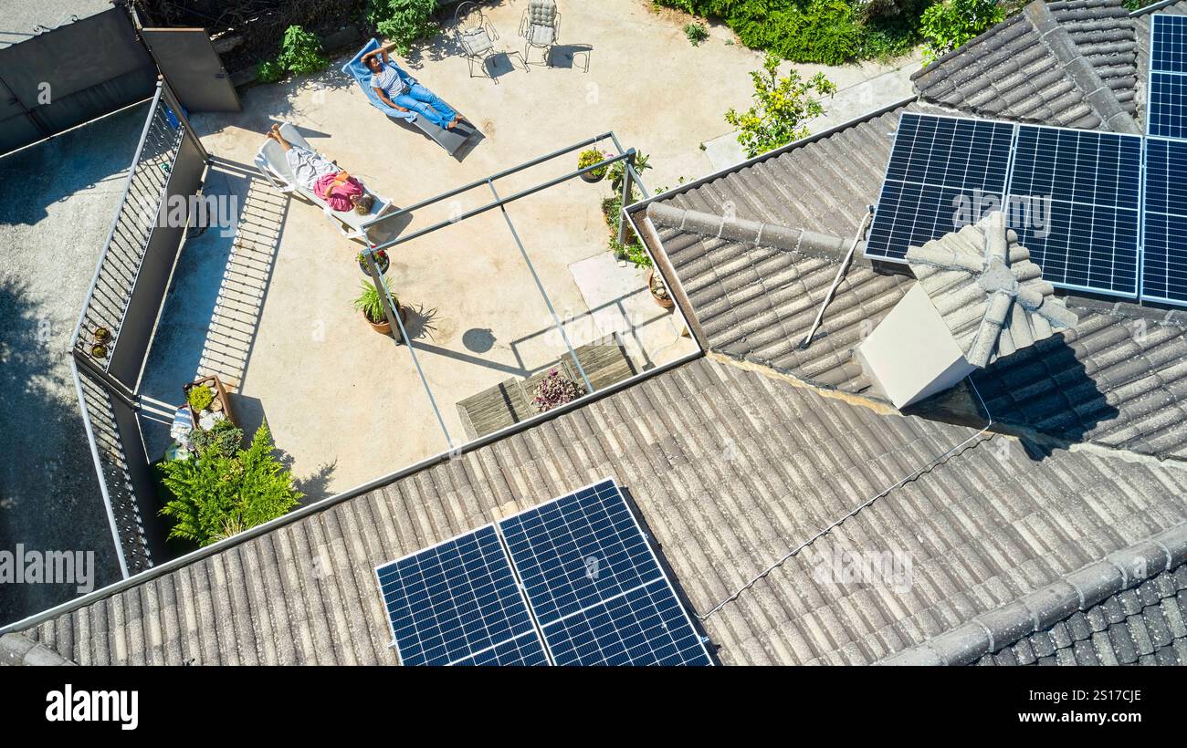 Une vue aérienne montre deux femmes bronzer dans une cour ensoleillée tandis que des panneaux solaires sont installés sur le toit. La scène met en évidence l'éco-responsable et Banque D'Images