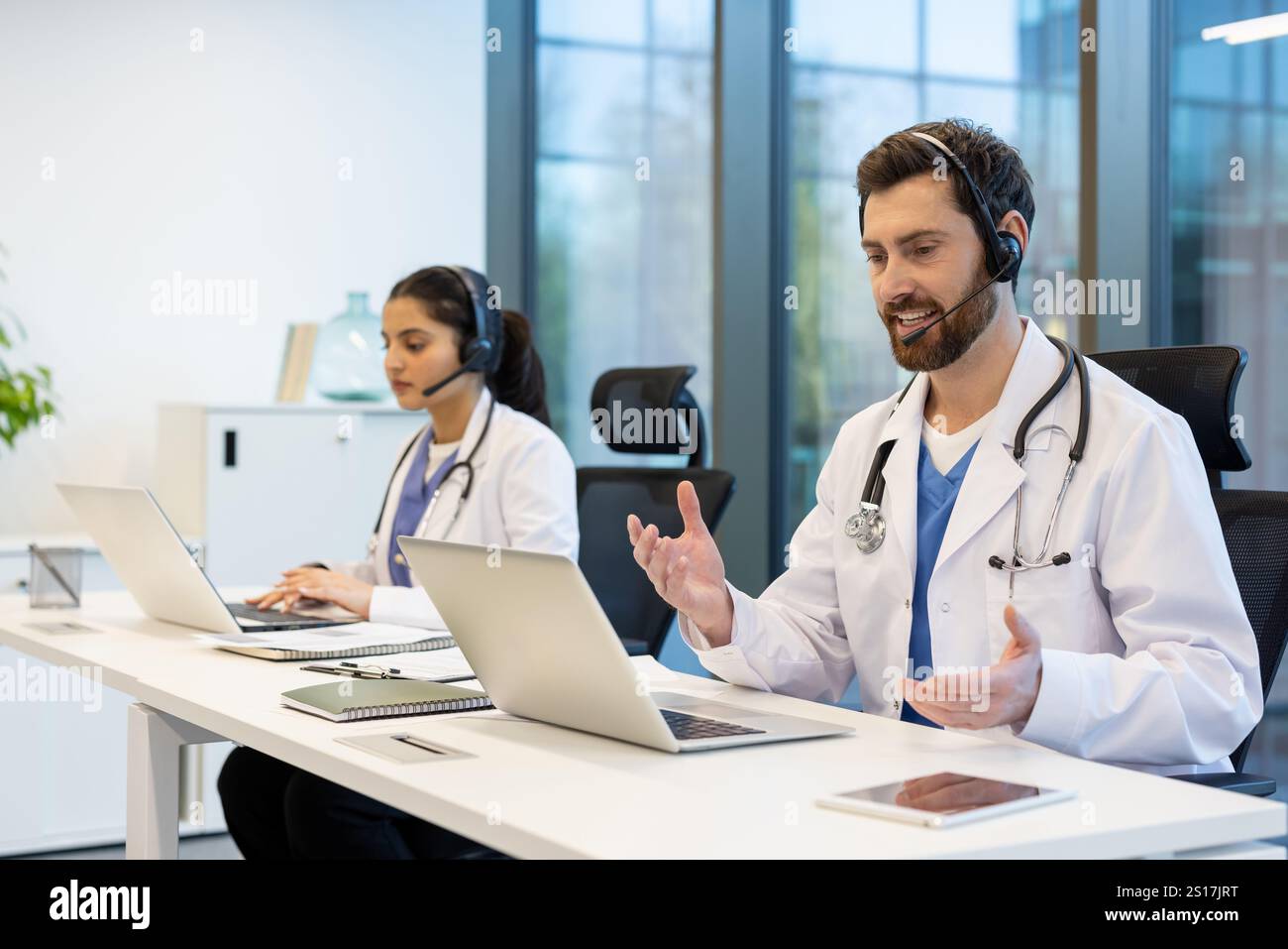 Deux médecins travaillant à distance consultant les patients à distance, homme et femme avec casque à l'aide d'un ordinateur portable pour l'appel vidéo, travaillant à l'intérieur de la clinique, le soutien aux patients et le service d'assistance. Banque D'Images